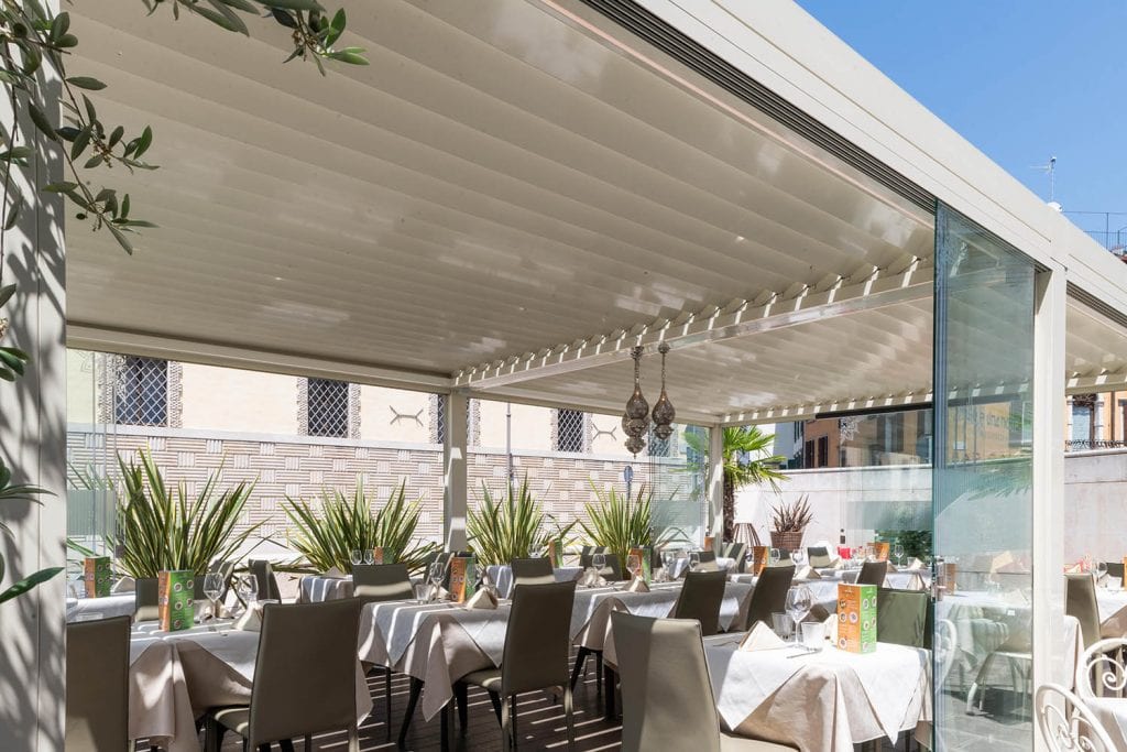 Bioclimatic pergola with adjustable sunscreen blades to protect seats in a bar or restaurant from sun and rain