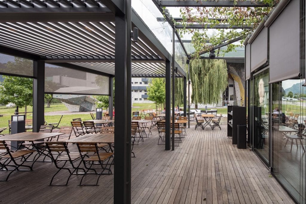 Bioclimatic pergola with adjustable sunscreen blades to protect seats in a bar or restaurant from sun and rain